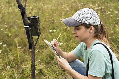 Woman scientist zoologist writing down data from trap camera to notepad, observing wild animals 