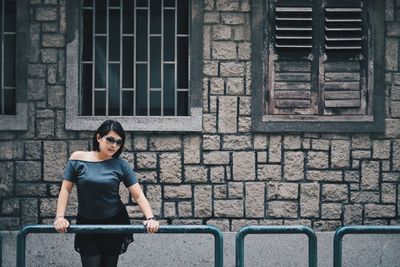 Woman leaning on railing while standing against old building