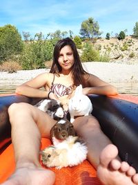 Portrait of young woman with pets sitting in inflatable raft on lake during sunny day