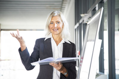 Leader manager older woman standing with book near flipchart