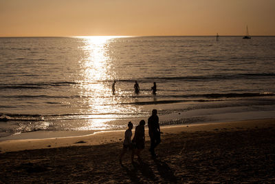 Silhouette people on beach against sky during sunset