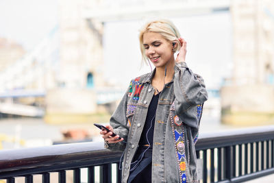 Young woman listening music while standing by railing in city