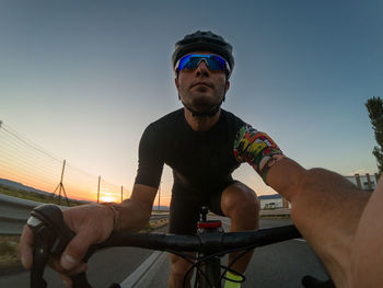 Low angle view of man cycling against clear sky during sunset
