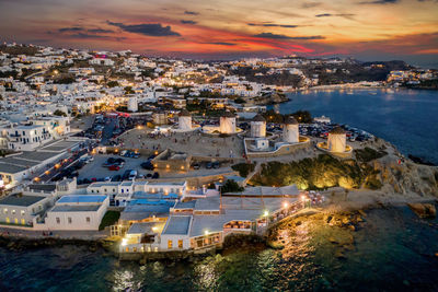 Aerial view of illuminated cityscape by sea against sky during sunset