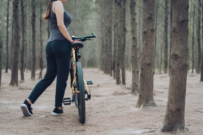 Low section side view of sporty woman standing with bicycle in forest
