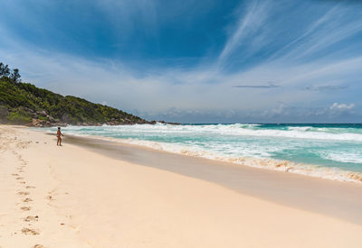 Woman standing alone on tropical sandy beach with idyllic turquoise ocean and waves