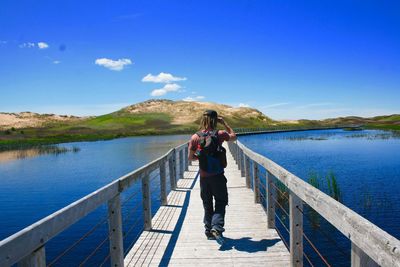 Rear view of man walking on pier over blue lake