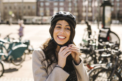 Happy businesswoman wearing helmet at bicycle parking station in city