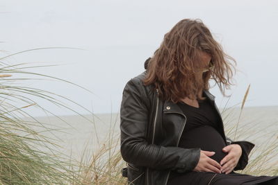 Pregnant woman sitting at beach against sky