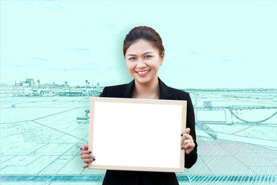 Portrait of smiling woman holding picture frame against sky