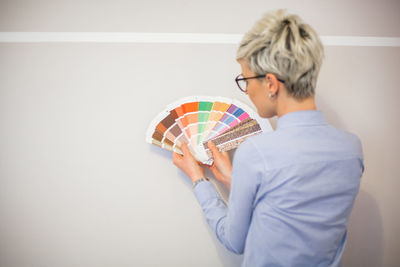 Rear view of woman holding color swatch against wall