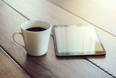 Close-up of coffee cup by digital tablet on table