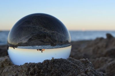 Close-up of crystal ball on rock at beach against sky