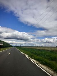 Country road by field against sky