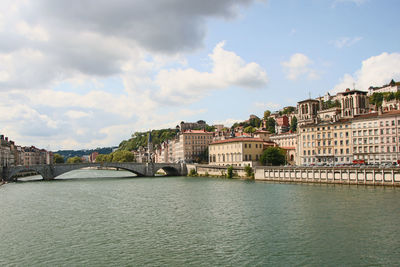 View of buildings by river against cloudy sky