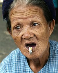 Close-up of senior woman smoking cigarette while sitting outdoors