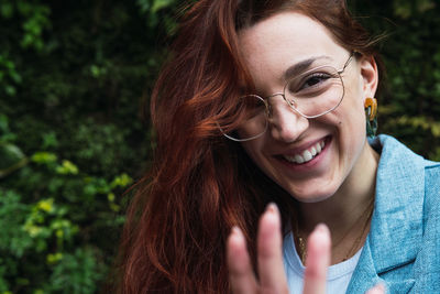 Portrait of smiling natural woman with long red hair pulling hand towards camera while having fun