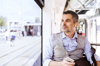 Businessman with smartphone and earphones travelling in tram