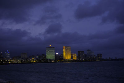 Illuminated buildings by sea against sky at night