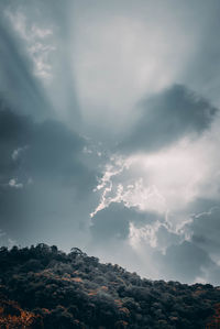 Low angle view of sunlight streaming through clouds