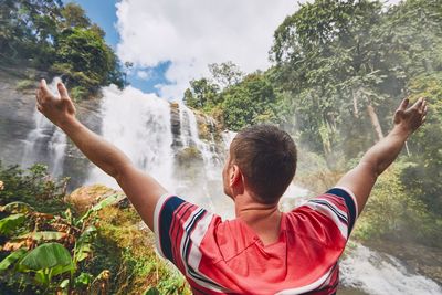 Rear view of man standing against waterfall