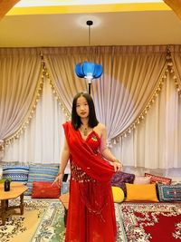 Portrait of young woman standing against curtain