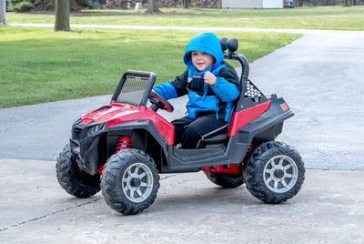 A cute little boy waves as he drives a battery powered jeep down the driveway