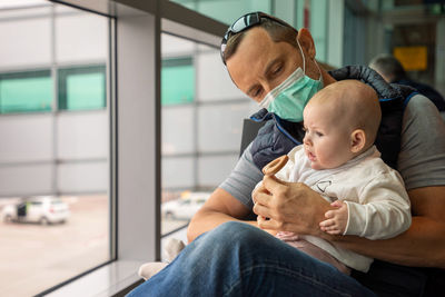 Father wearing mask sitting at airport with daughter