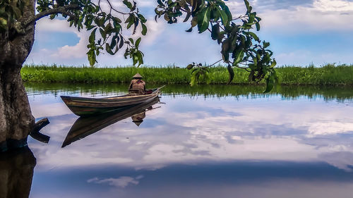 Man sitting in boat on lake against sky