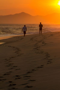 People walking on beach against sky during sunset