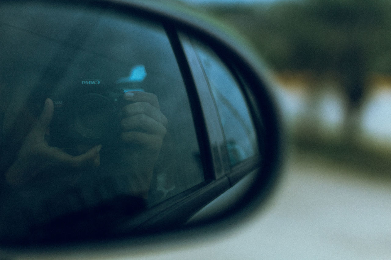 REFLECTION OF MAN PHOTOGRAPHING IN CAR MIRROR