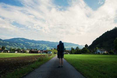 Rear view of man walking on road against sky