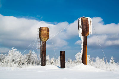 Low angle view of wooden post on snow covered field against sky