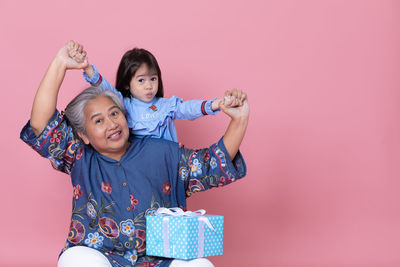 Portrait of grandmother holding granddaughters hands against pink background