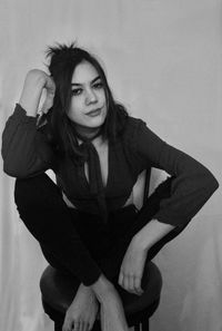 Portrait of young woman sitting on seat against wall