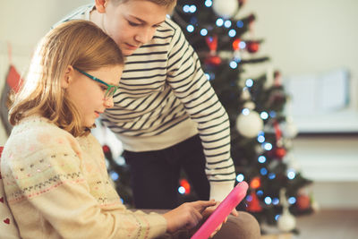 Siblings using digital tablet at home during christmas
