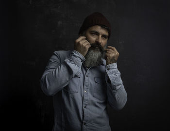 Portrait of handsome smiling man with beard sticking his mustache jeans shirt and wool hat.