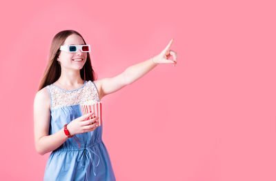 Young woman wearing sunglasses standing against gray background