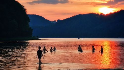 Silhouette people on lake against orange sky