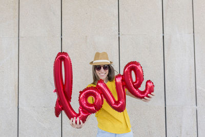 Portrait of woman holding balloons with text while standing against wall