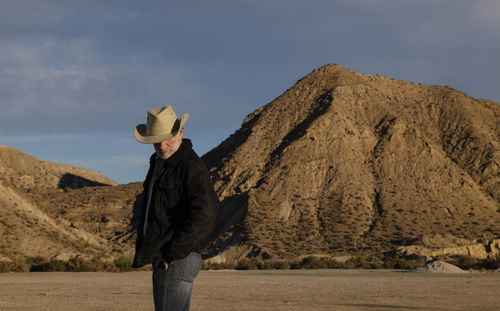 Adult man in cowboy hat standing against mountains in tabernas desert. almeria, spain