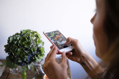 Cropped image of woman photographing food on table by vase at home
