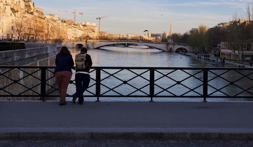 People on bridge over river against sky