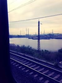 Railroad tracks by river against sky during sunset