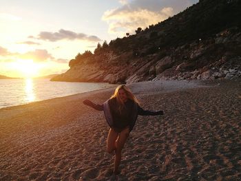 Woman dancing on sand against sky during sunset