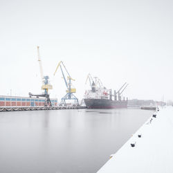 Cranes at harbor against clear sky