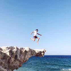 Man jumping from rock in sea