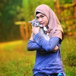 Portrait of teenage girl holding cat while kneeling on grassy field