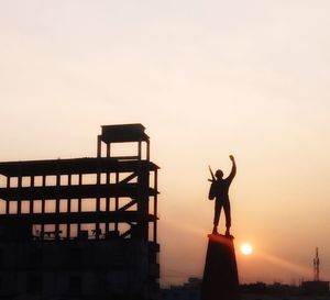 Silhouette man with arms raised standing against sky during sunset