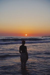 Rear view of woman standing on beach during sunset